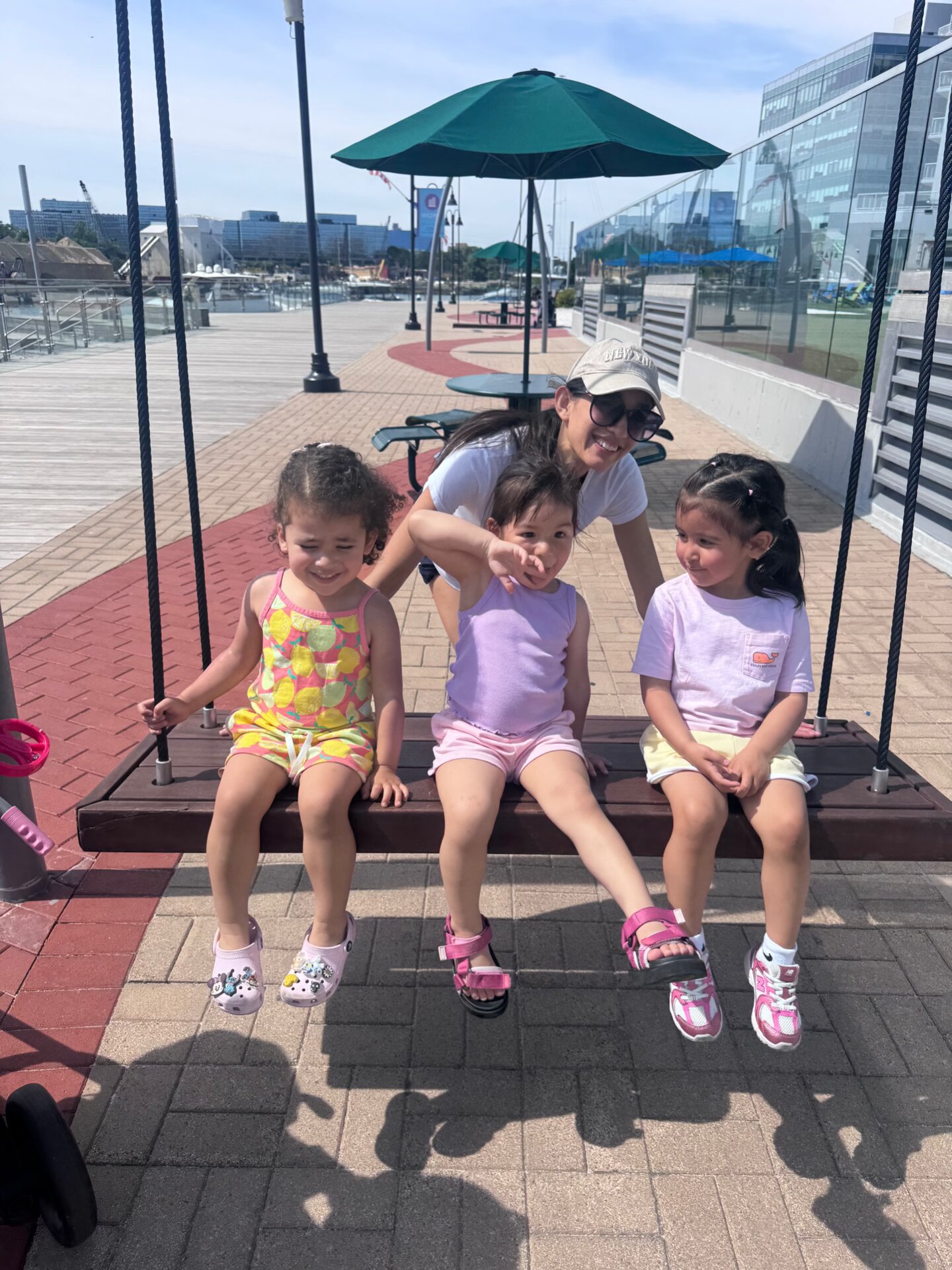 Three little girls on a swing bench at Harbor Point with the harbor behind them