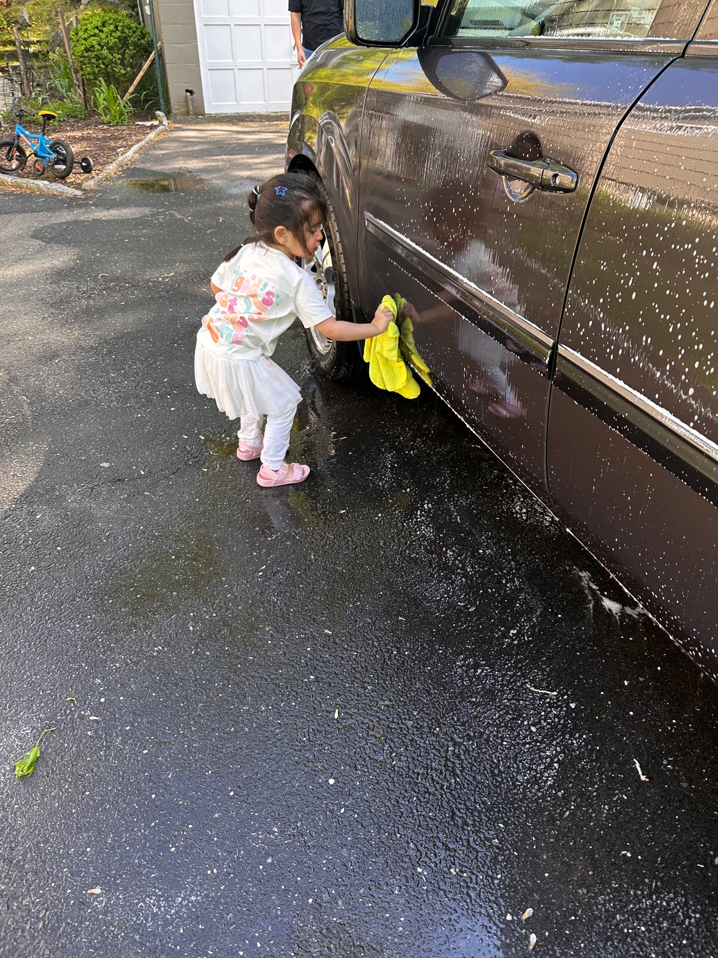 Little girl helping wash the family car in the driveway