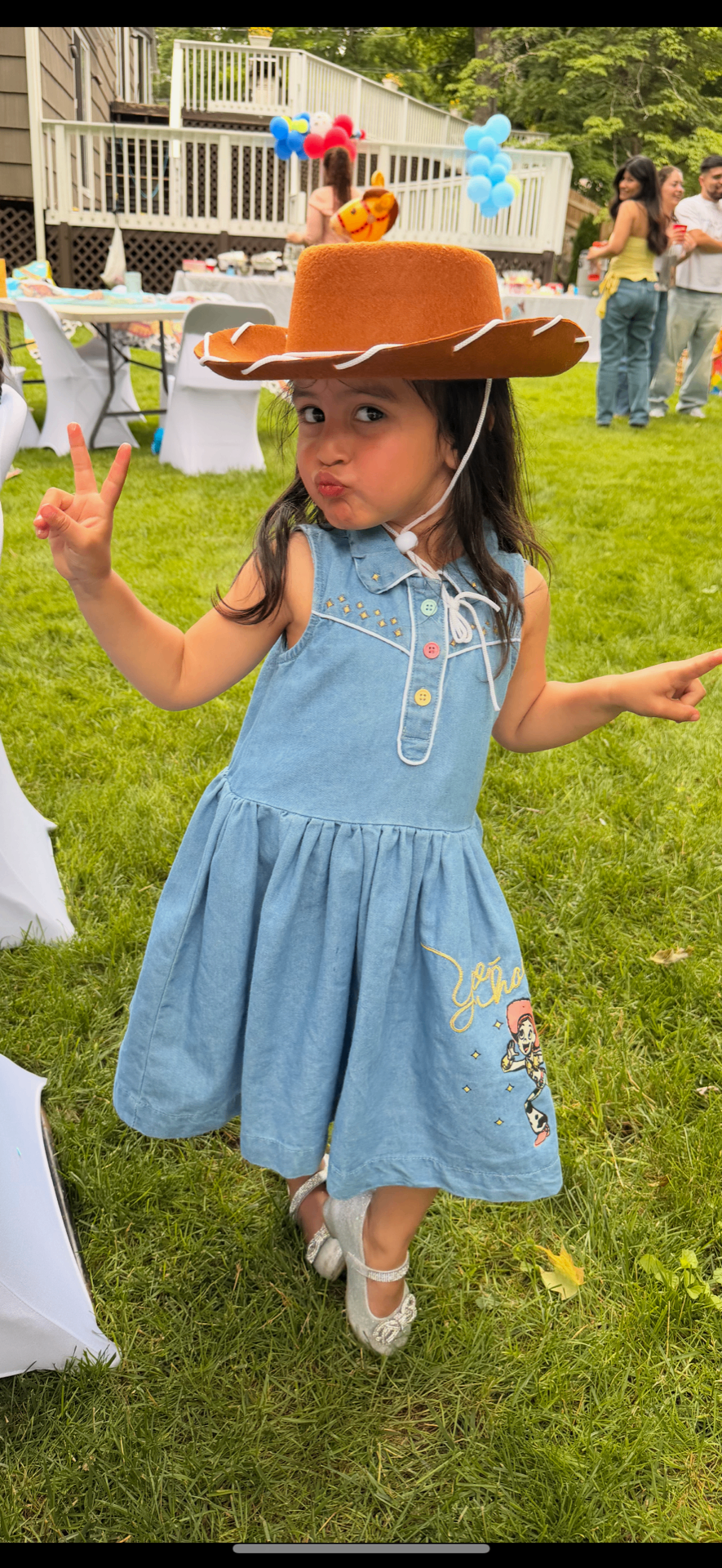 Little girl in a cowgirl hat and denim dress posing at a backyard birthday party